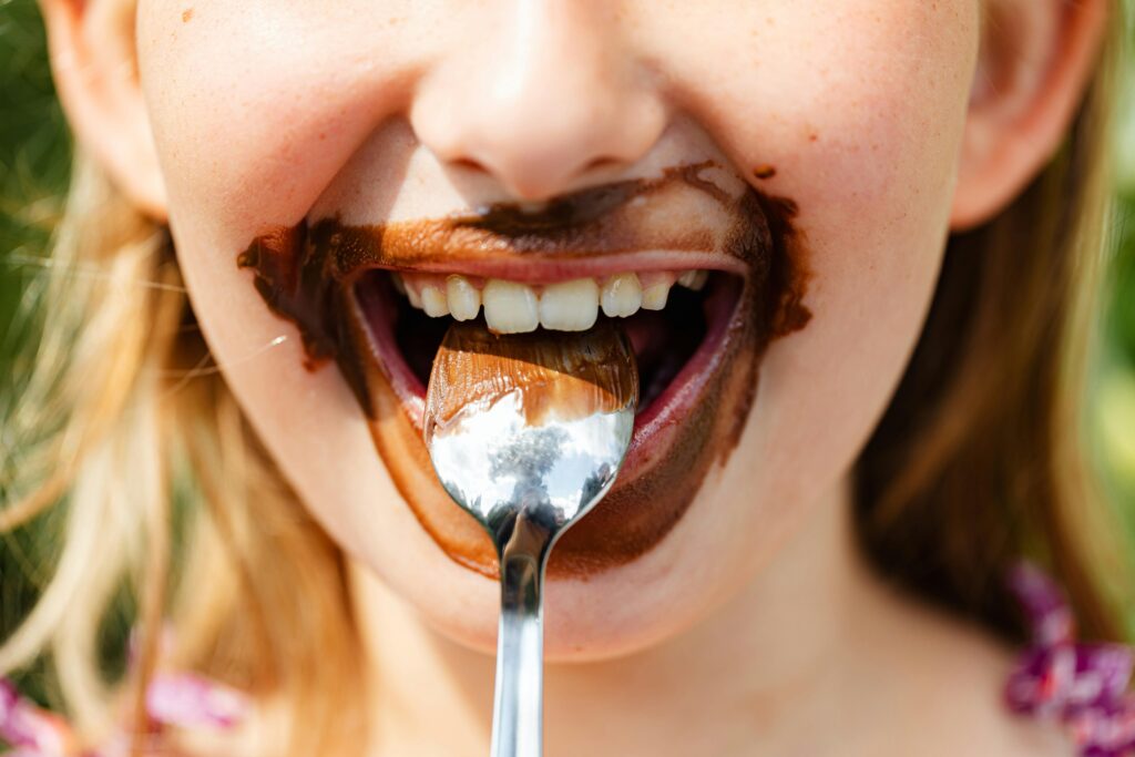 Close-up of a child's face enjoying a messy chocolate treat, smiling with a spoon.