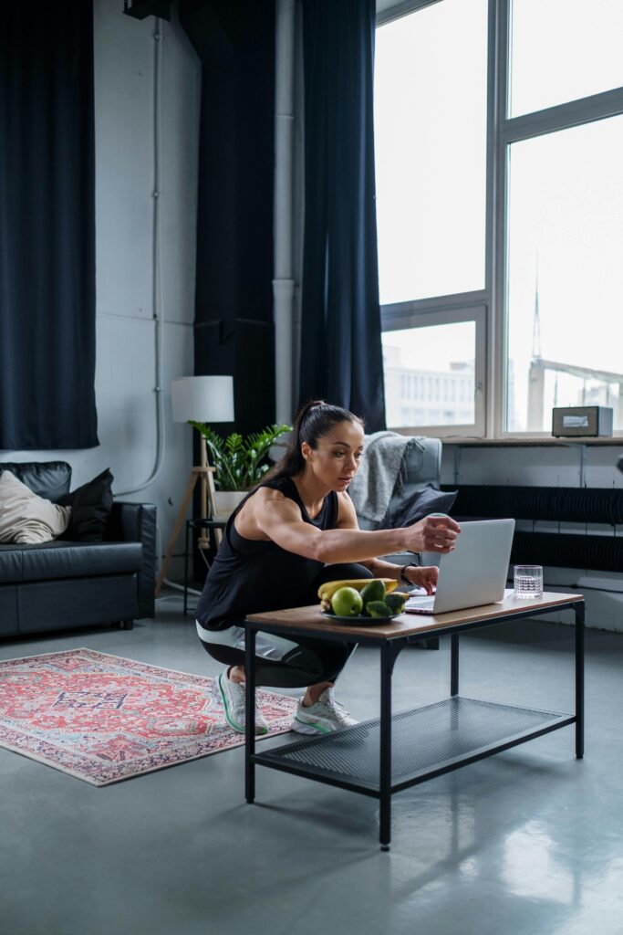 Woman using laptop while exercising at home, featuring a modern gym setting.